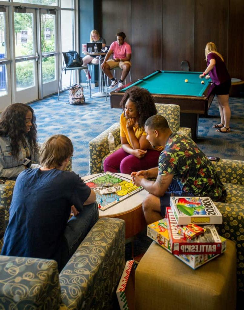 A group of student in a room speaking and playing pool.